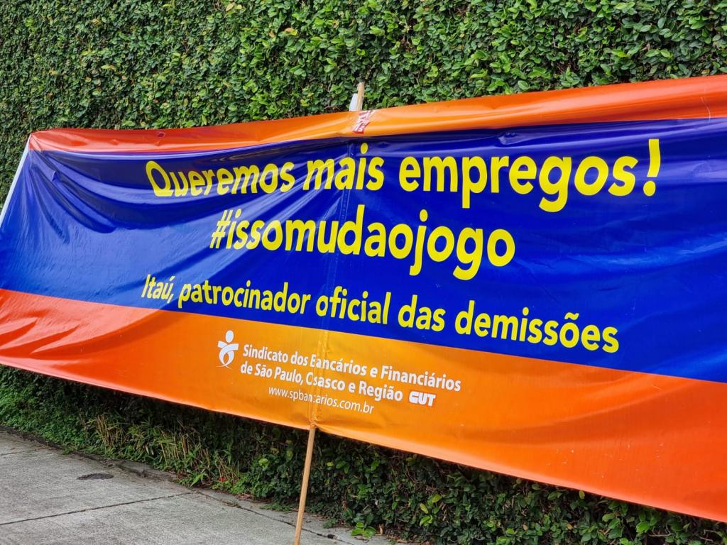 Foto mostra uma faixa com os dizeres "Queremos melhores condições de trabalho #issomudaojogo. Itaú, patrocinador oficial de metas abusivas"
